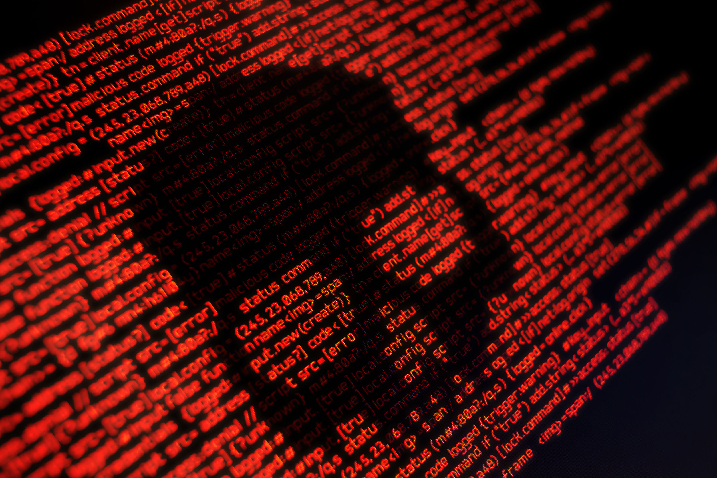 Red programming code displayed on a dark screen, forming the silhouette of a skull, symbolising cyberthreats.